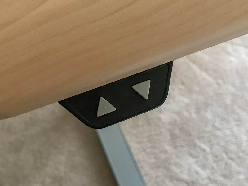 A small plastic enclosure contains the two buttons. The enclosure is mounted directly underneath the desktop. Both buttons are next to each other, but with ample space between them to prevent pressing the wrong one by mistake.